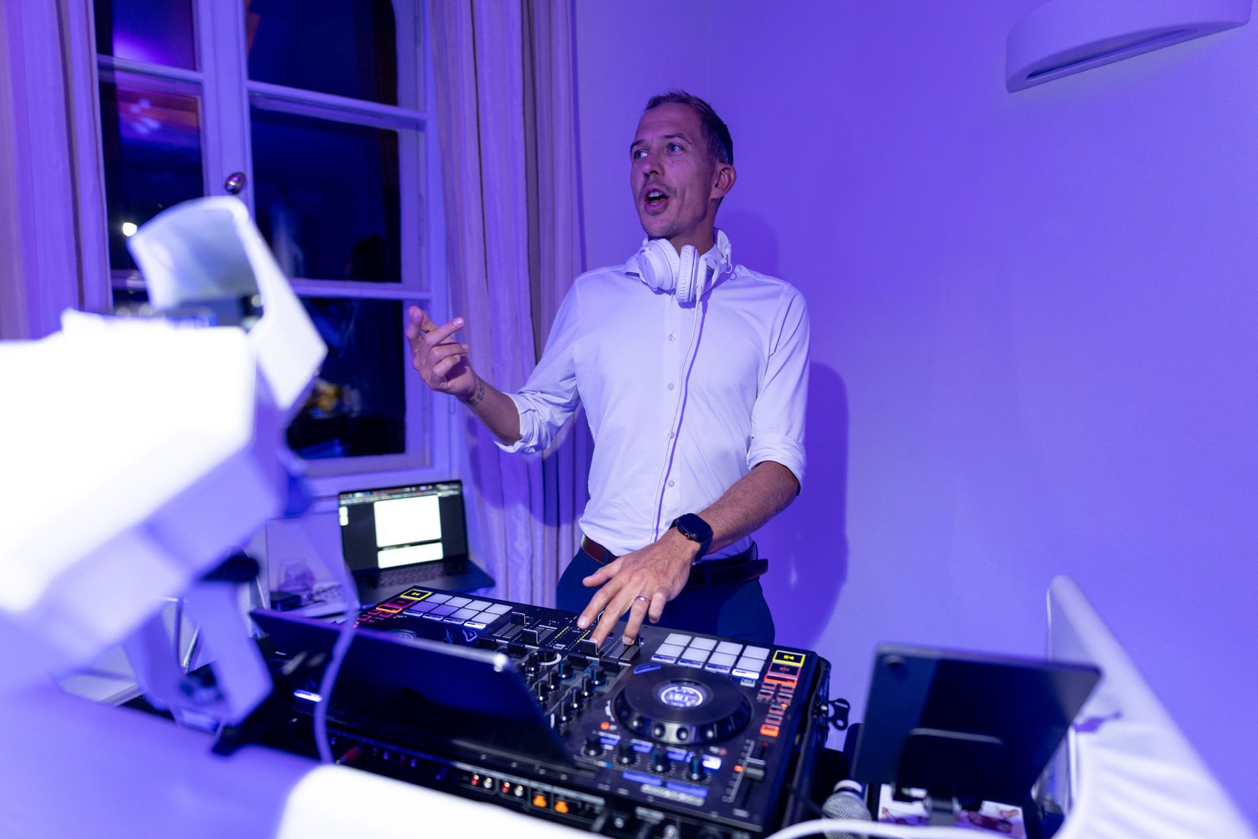 Chris Carter am weißen DJ-Pult in violettem Licht, mit Kopfhörern um den Hals