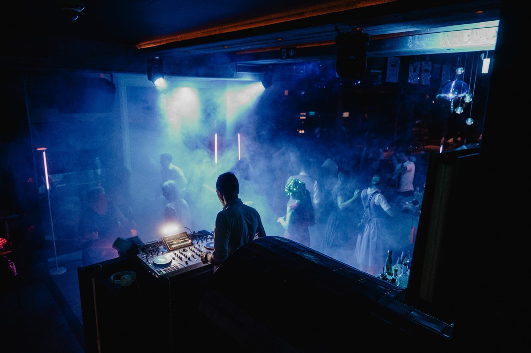 Blick über Chris' Schulter auf die volle Tanzfläche, Nebel, blaue Deckenspots, Lichtstange, starke Partystimmung