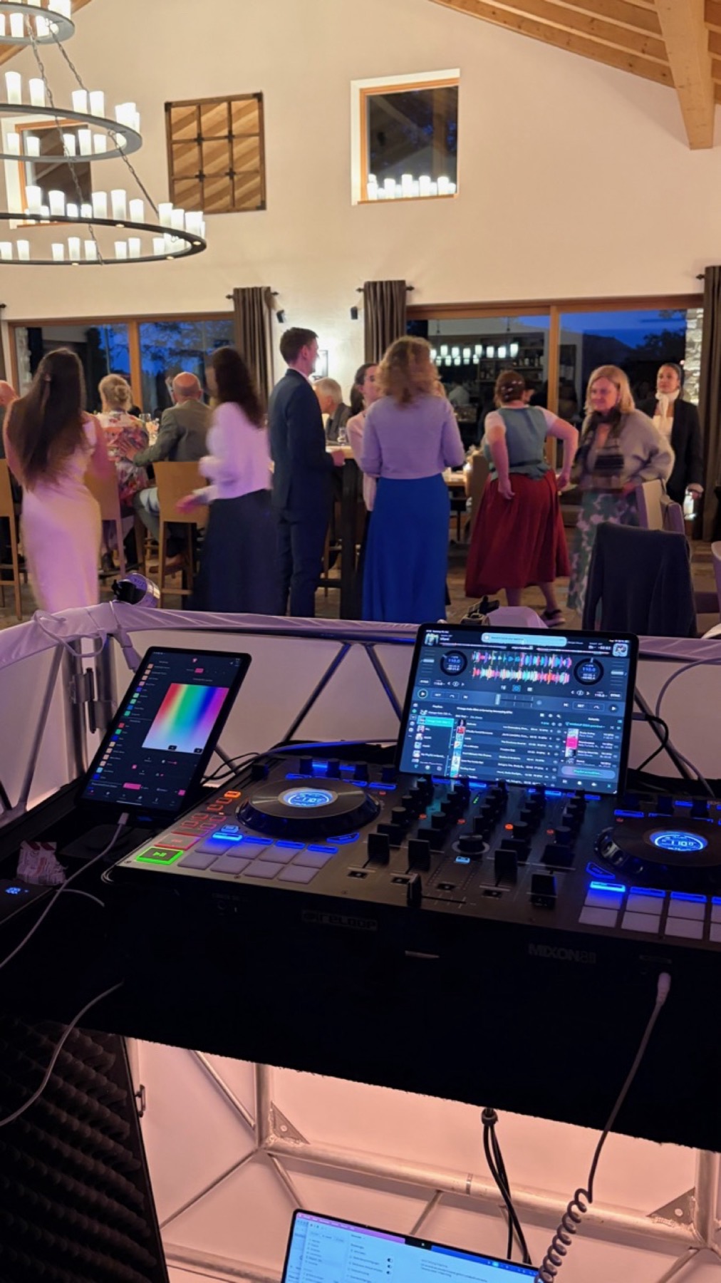 DJ-Pult mit Bildschirm, davor tanzende Gäste im Saal