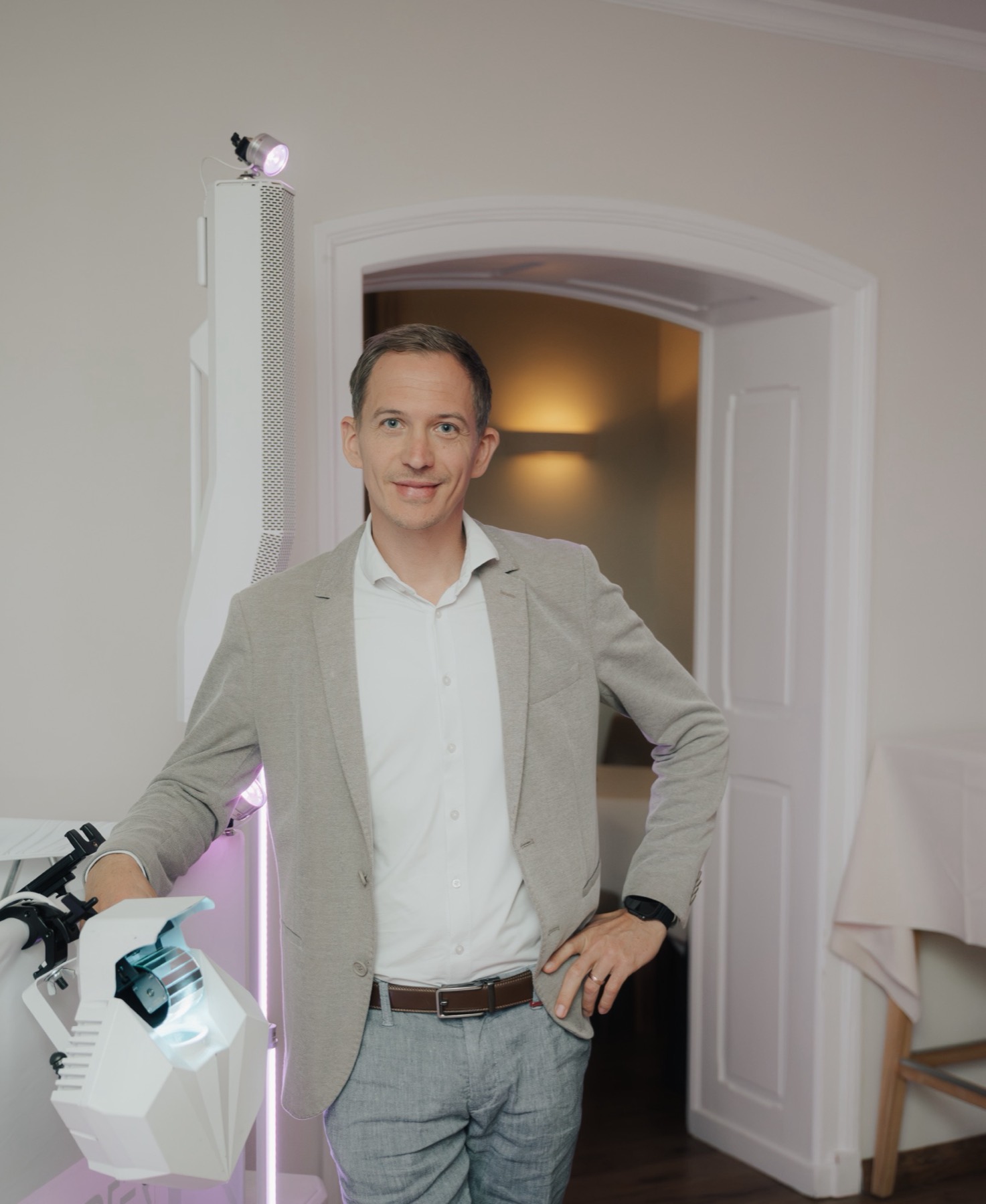 Portrait im hellen Sakko, angelehnt an weißen Säulenlautsprecher mit Moving Head und Lichtstange, Türbogen dahinter