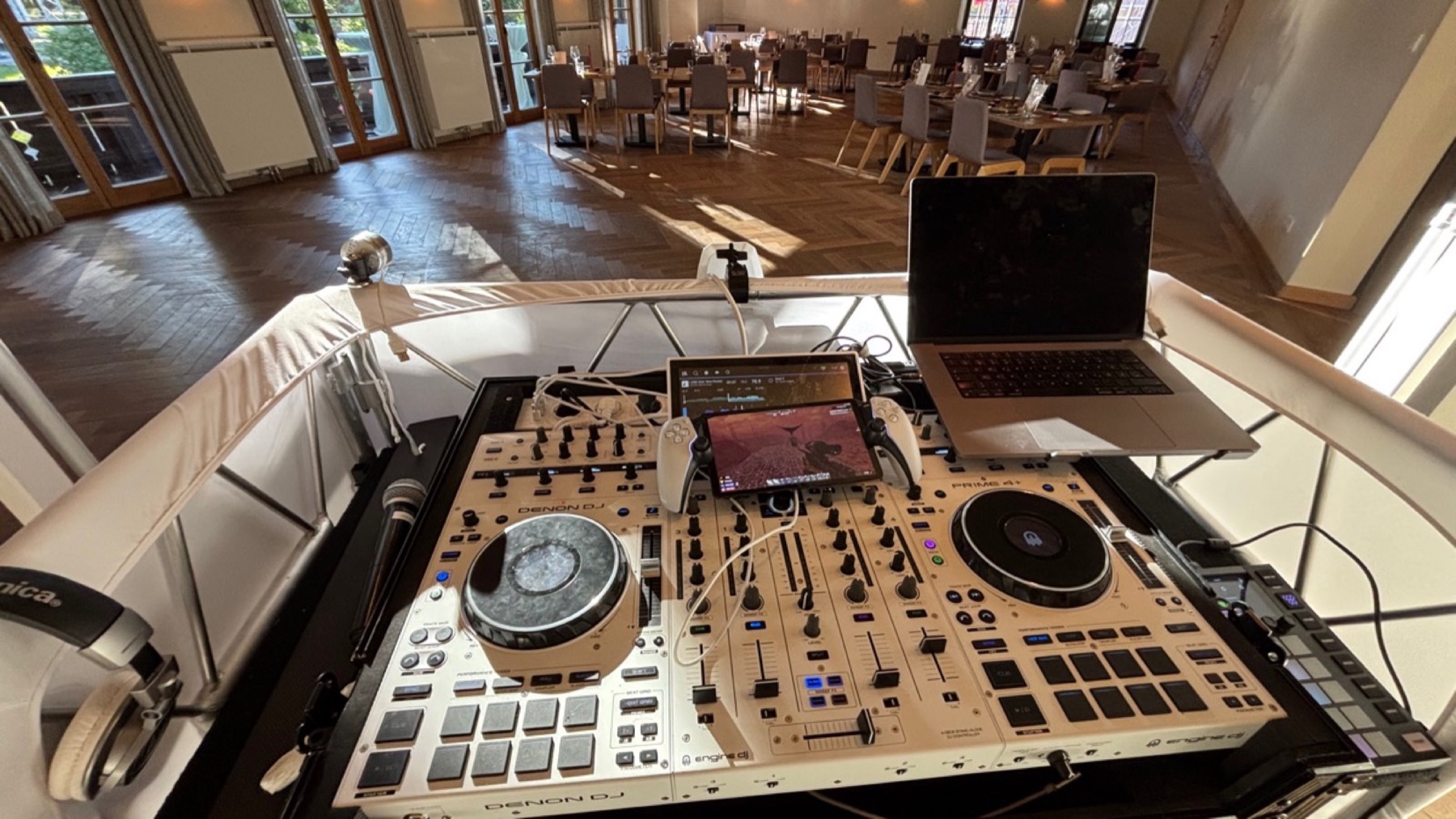 DJ-Pult mit Laptop und Mikrofon vor einem leeren, hellen Festsaal beim Aufbau