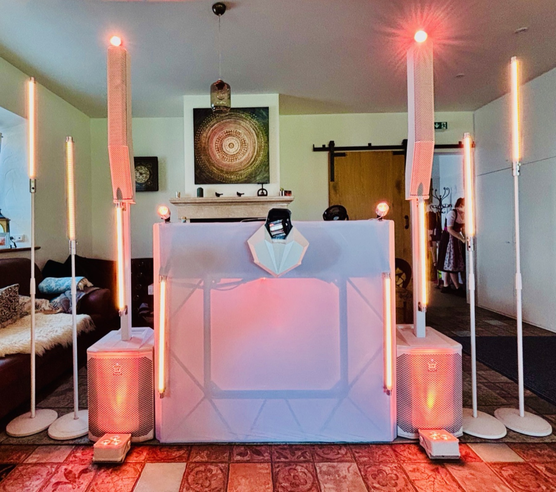 Weißer DJ-Pult mit zwei Säulenlautsprechern, Lichtstangen und warmen Spots im Partyraum