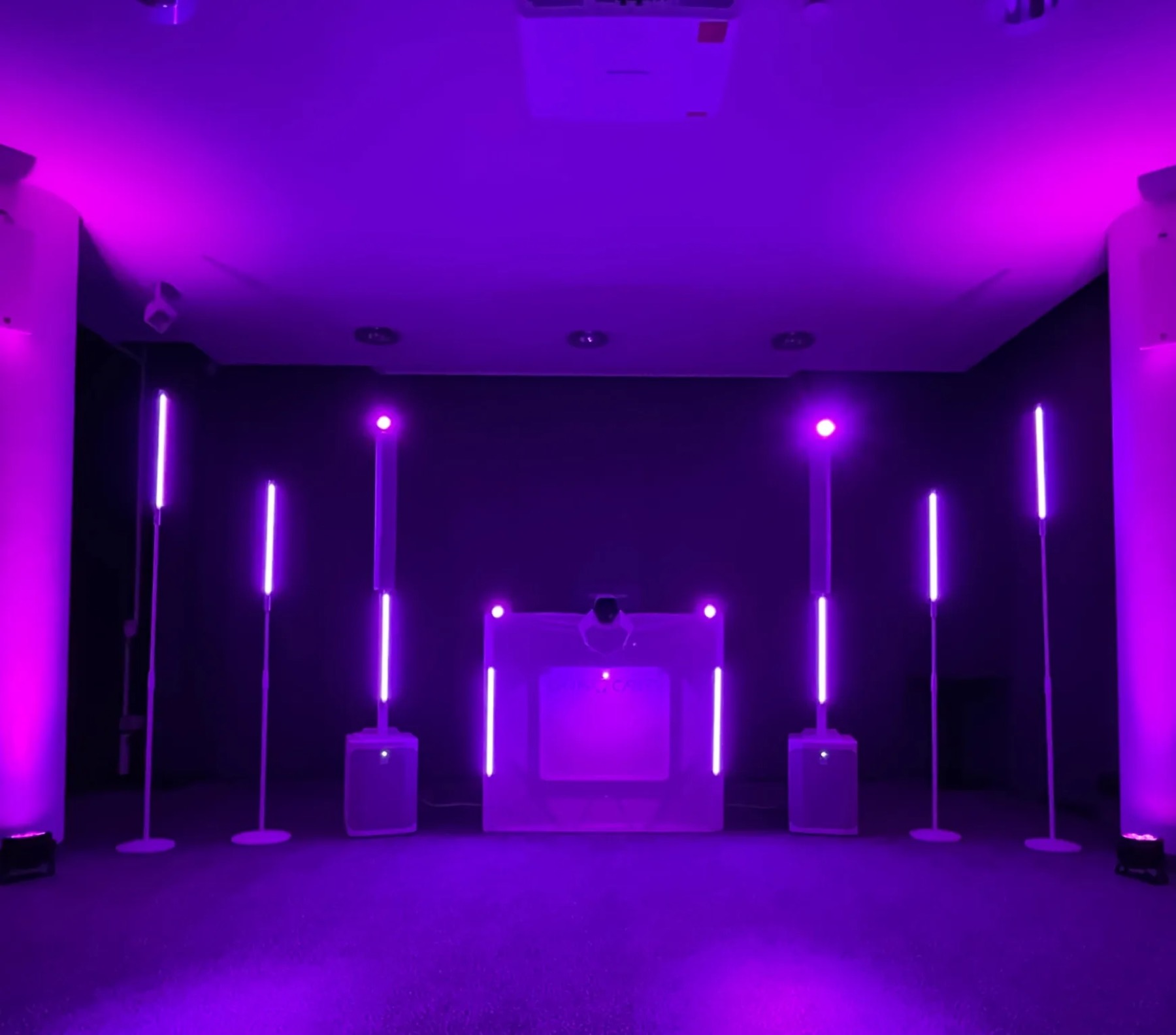 Weißes DJ-Setup mit Lichtstangen, Uplights an den Säulen, Raum in Violett