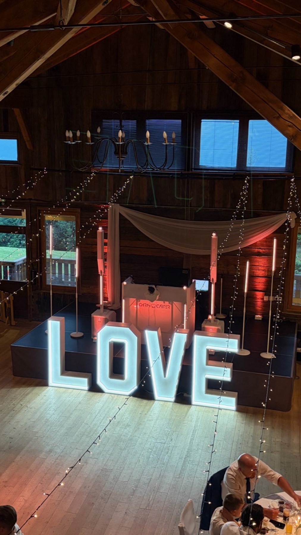 Holzscheune am Abend, DJ-Pult hinter leuchtenden LOVE-Buchstaben, Balken und Fenster rot angeleuchtet