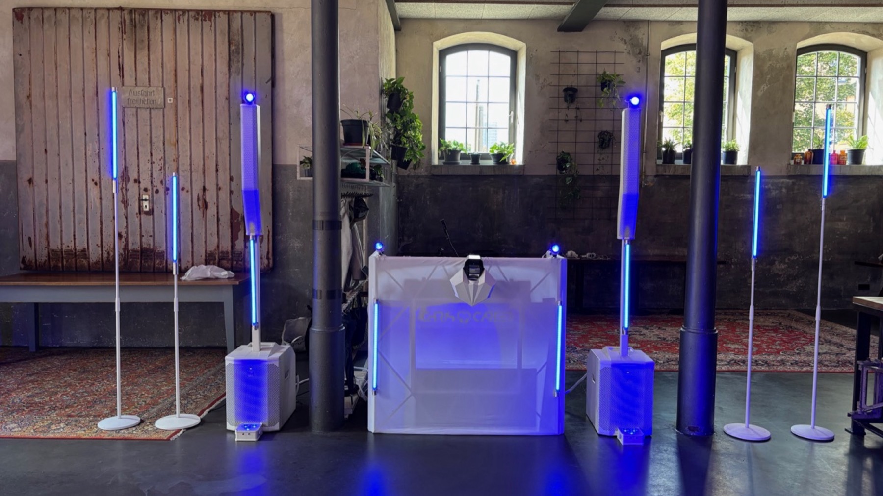 Weißer DJ-Pult mit Lautsprechern und blau leuchtenden Lichtstangen in einem Gewölbesaal