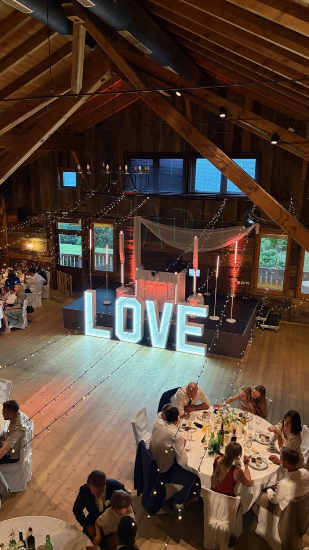 Scheune von der Empore, Tanzfläche mit LOVE-Buchstaben und DJ-Pult, rote Uplights an den Holzsäulen