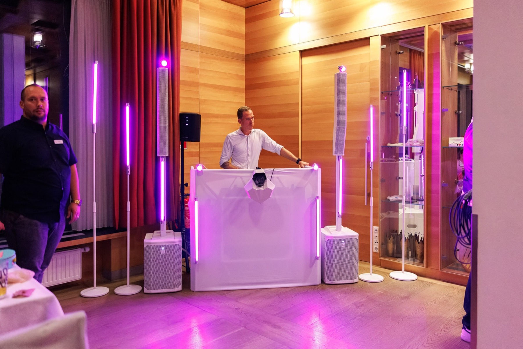 Chris am weißen Pult, zwei Säulenlautsprecher, sechs Lichtstangen in Pink