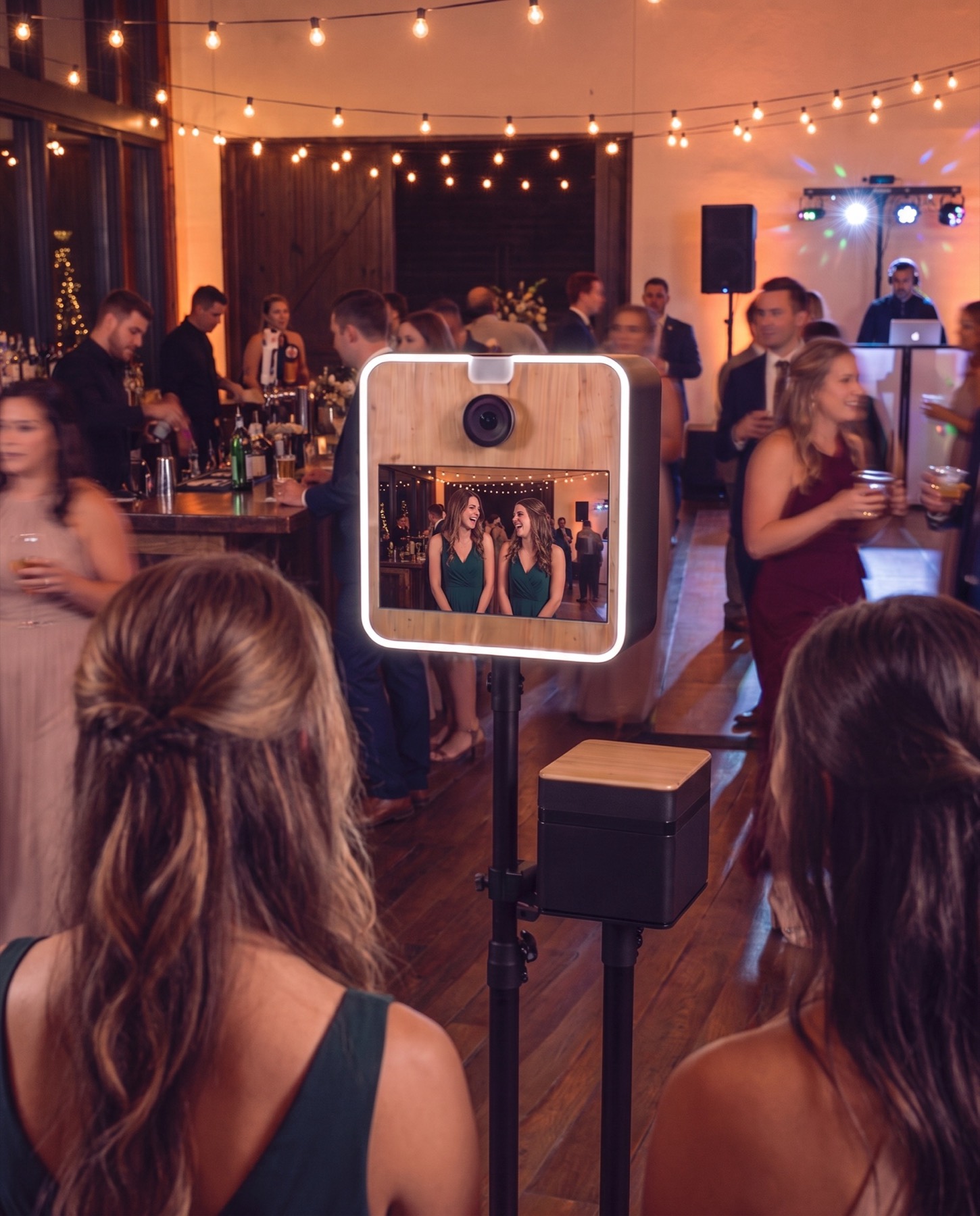 Hochzeitsgäste vor der Smilify Fotobox mit Eichenfront, im Hintergrund Bar und DJ-Pult