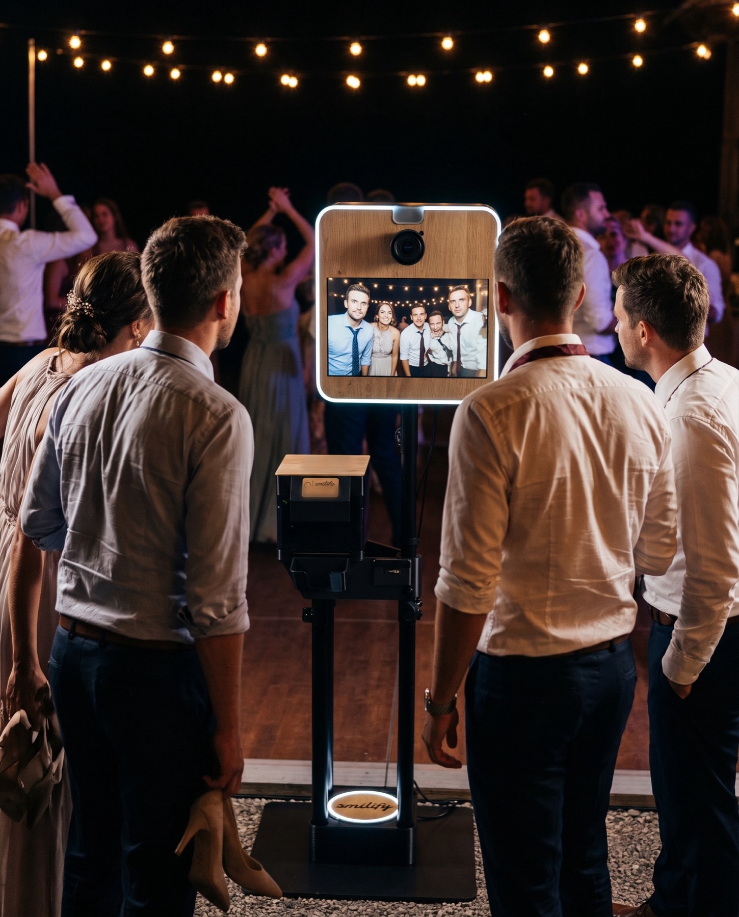 Trauzeugen und Gäste stehen nachts vor der Fotobox auf der Tanzfläche, der Monitor zeigt ihr Gruppenfoto
