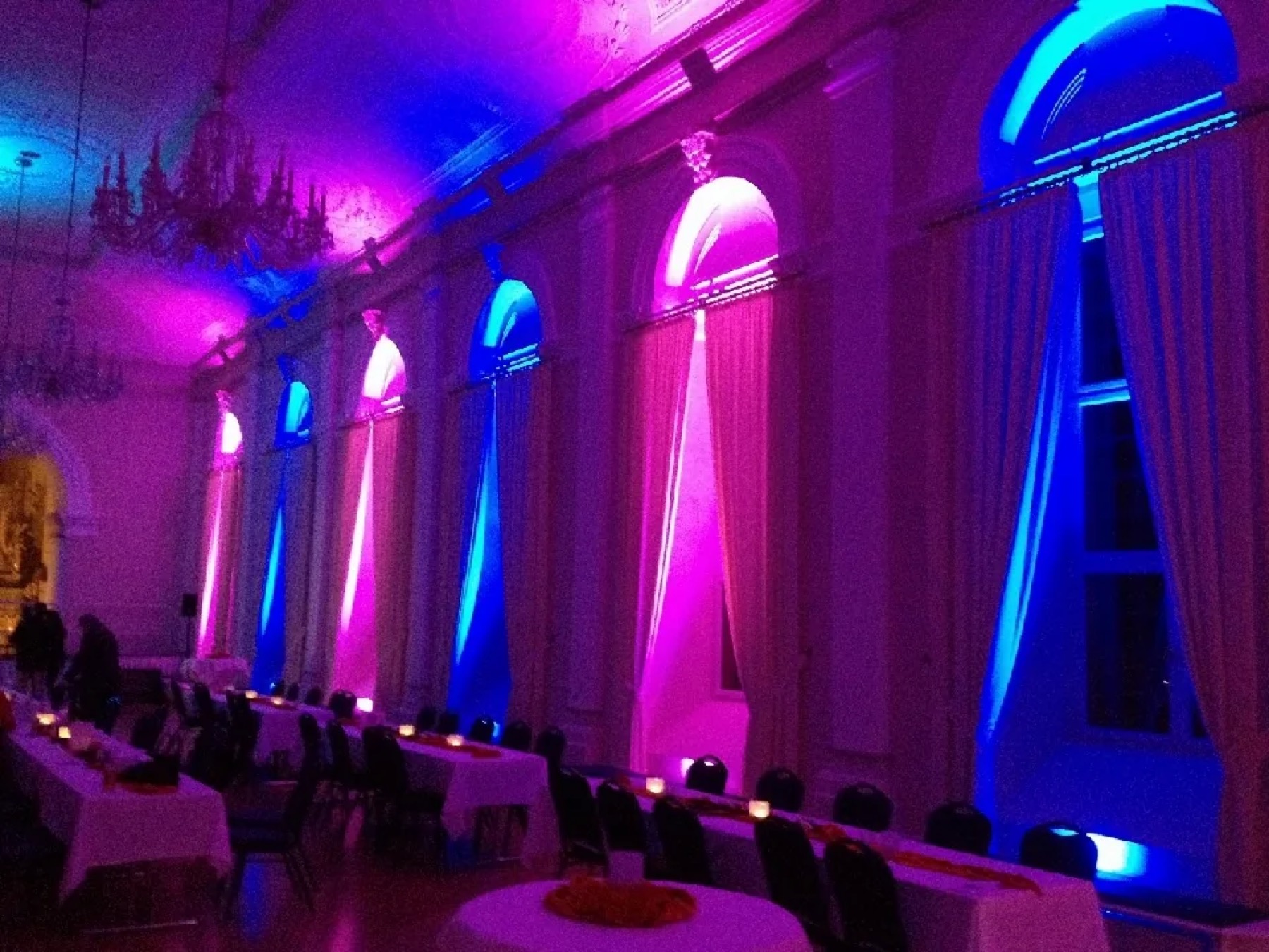 Festsaal mit Rundbogenfenstern, Uplights am Boden tauchen Fenster und Vorhänge in Blau und Pink