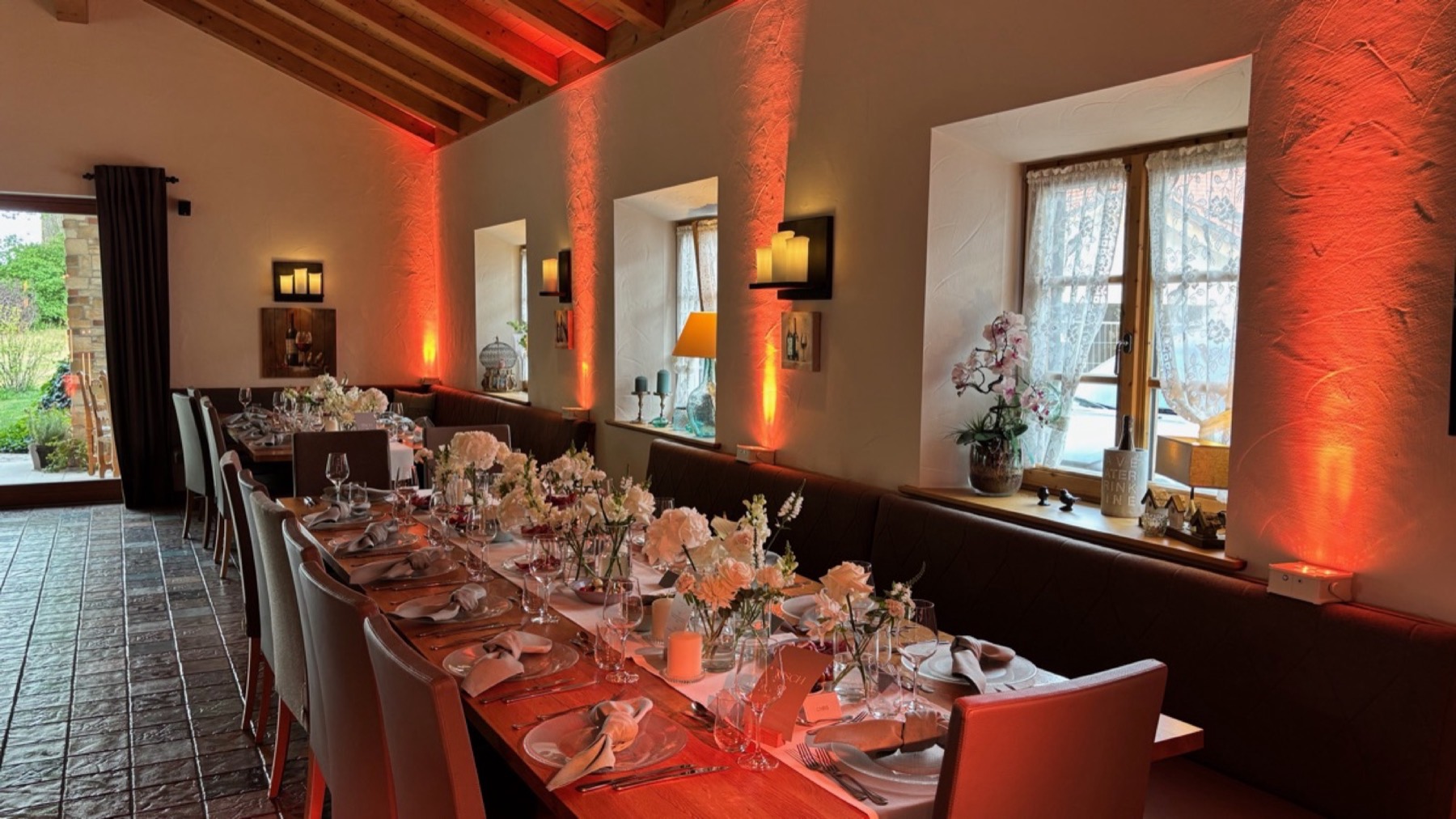 Festsaal mit langer Hochzeitstafel, Wände und Fensternischen in warmem Orange angeleuchtet