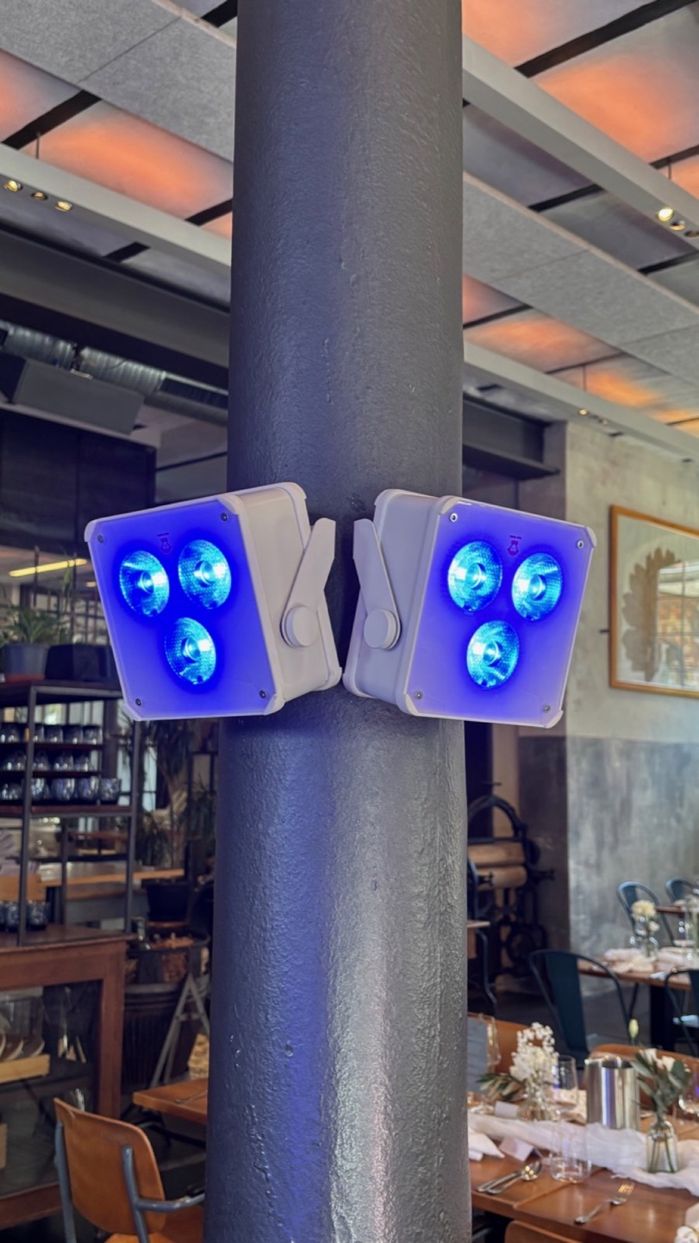 Zwei Akku-Uplights an einer Säule montiert, blau leuchtend, im Hintergrund die gedeckten Tische
