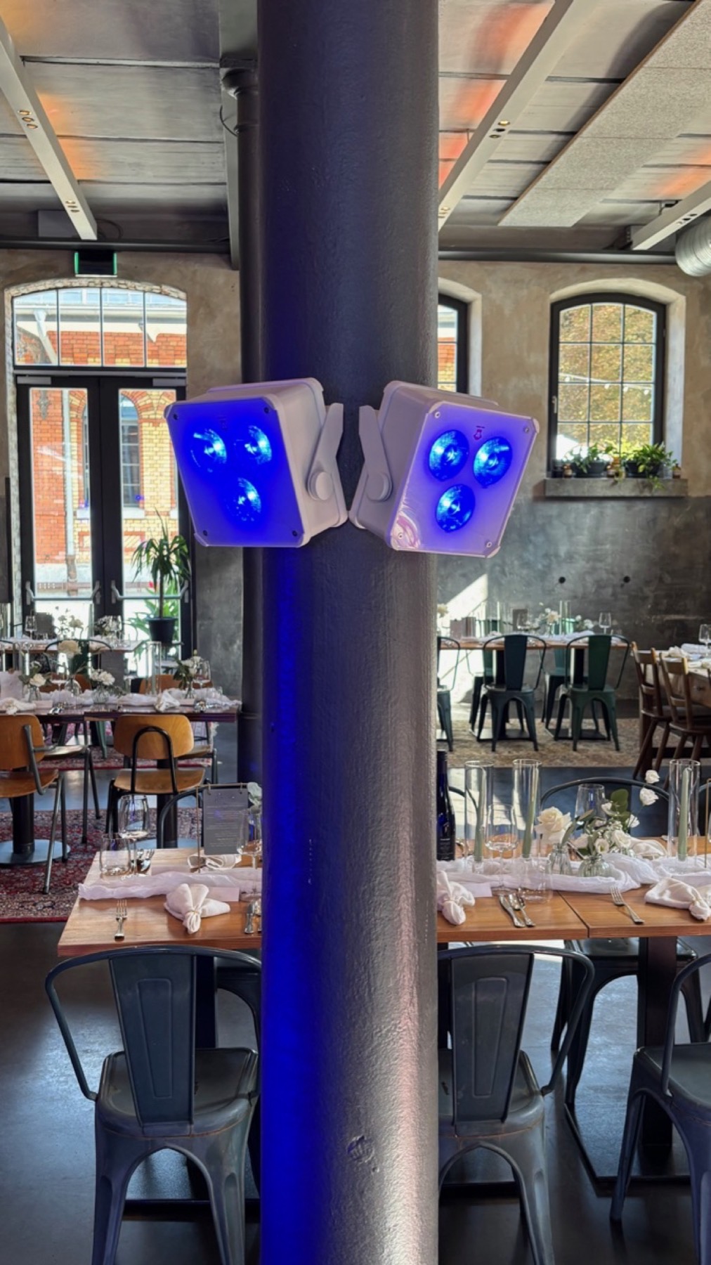 Uplights an einer Säule in einem Saal mit Industriecharme, blaues Licht, Tische im Hintergrund