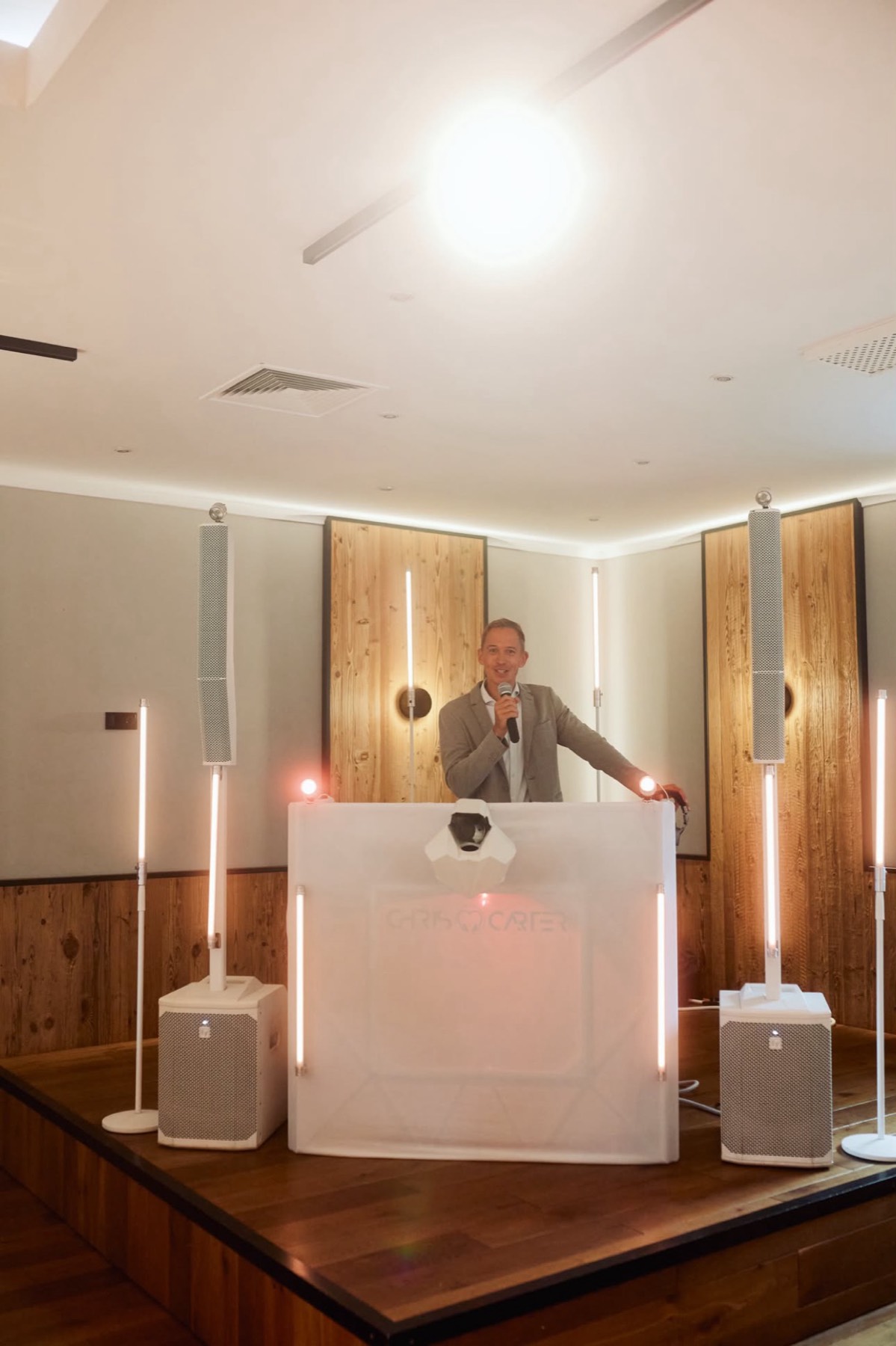 Weißes Pult mit Lichtsäulen auf einer Holzbühne, dahinter Chris Carter