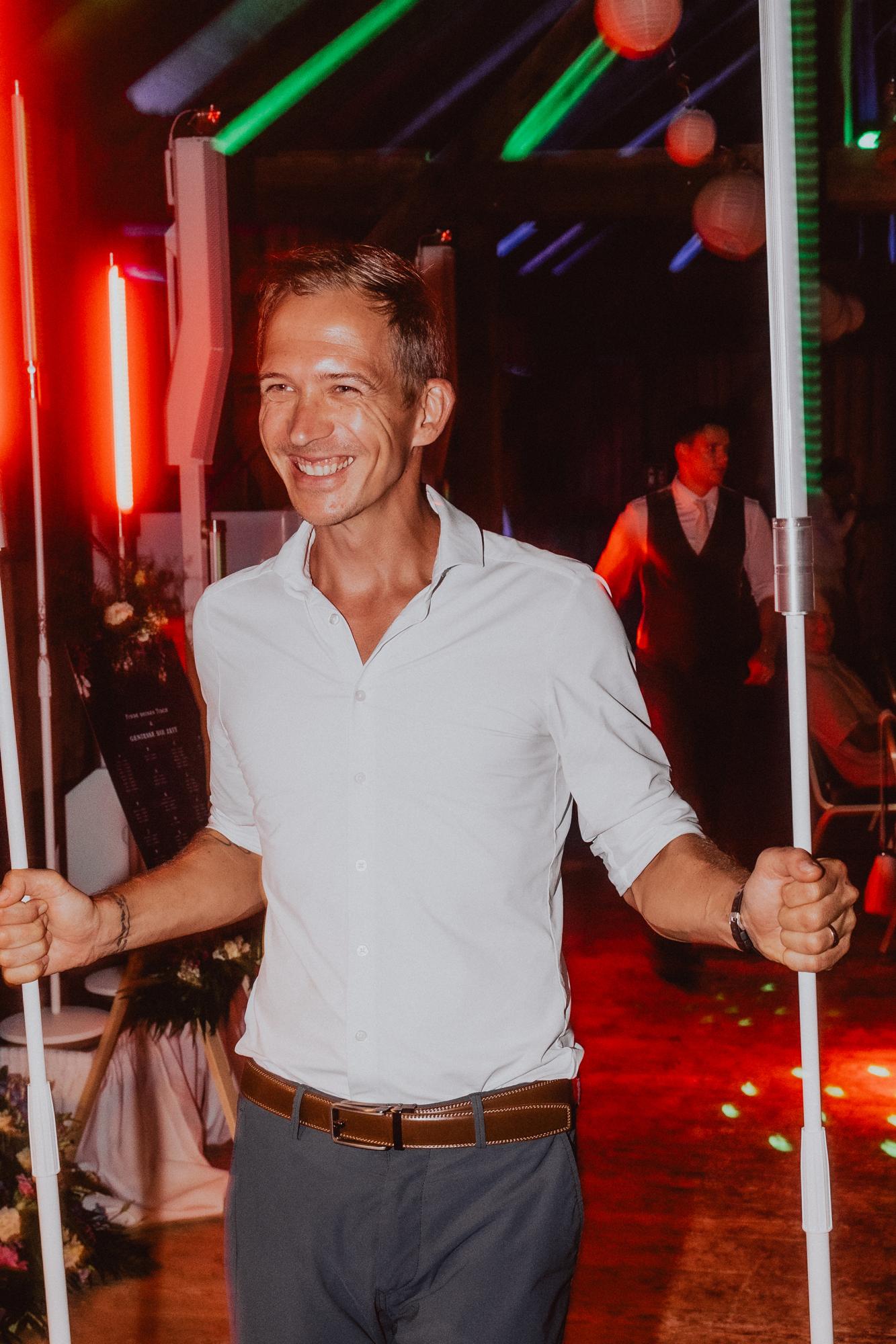 Chris Carter trägt lachend zwei leuchtende Lichtstäbe über die Tanzfläche