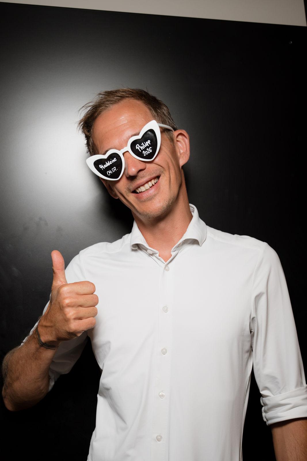 Chris Carter mit weißer Herzbrille hebt lachend den Daumen